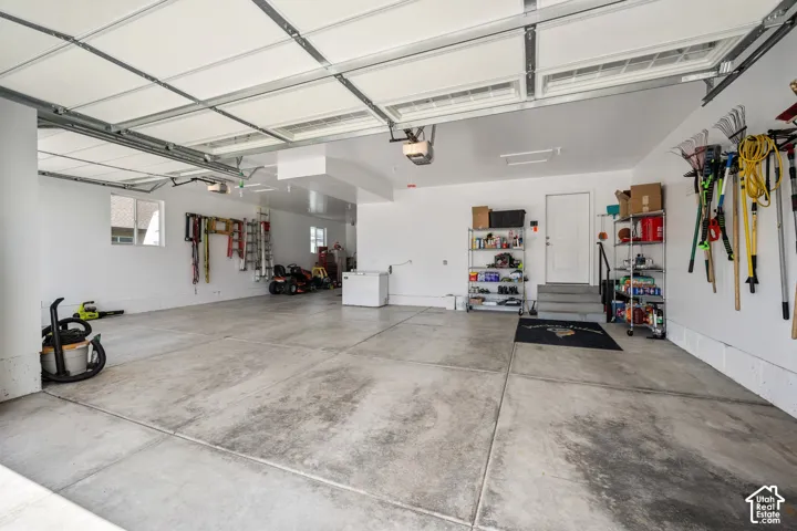 Spacious garage featuring polished concrete flooring, overhead lighting, wall-mounted storage and tool organization, and direct interior access to the home