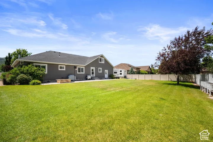 Expansive lawn with mature landscaping, a privacy fence, and a stone patio