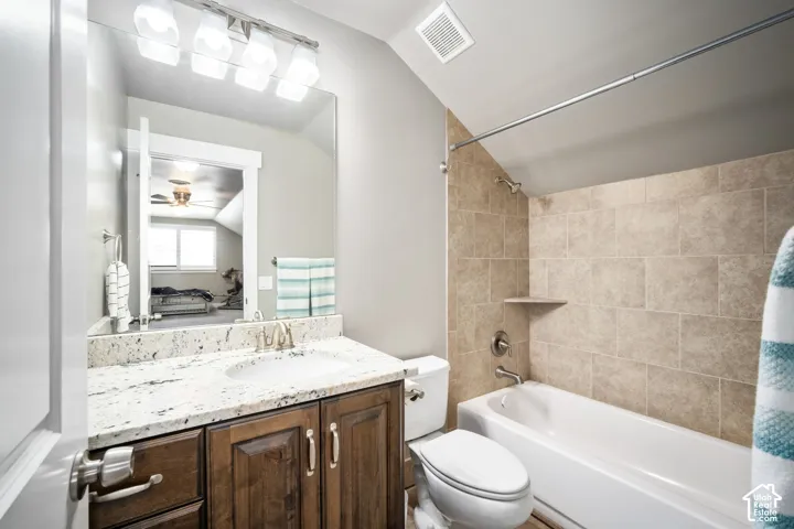 Integrated bathtub and shower with neutral-toned wall tiling, rich wood-finish vanity with a light-toned countertop, and an expansive mirror with overhead lighting