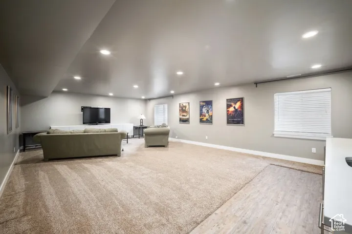 Spacious finished basement featuring recessed ceiling lighting, neutral carpet and wood-finish flooring, mounted flat-screen television, and abundant natural light from large windows