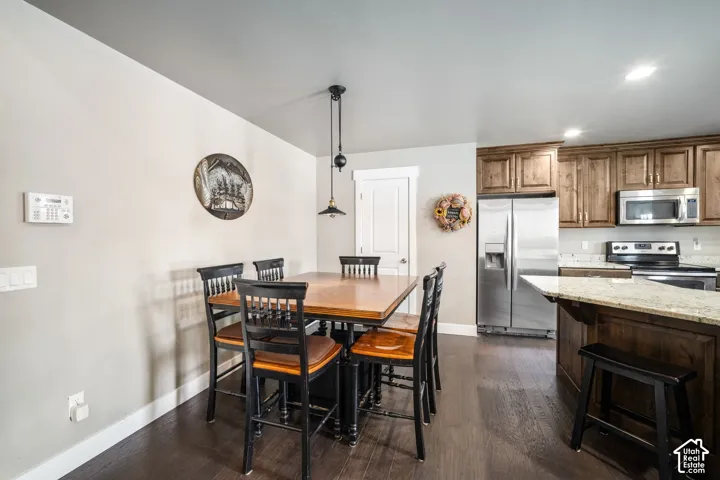 Open-concept kitchen and dining area featuring stainless steel appliances, wood-finish cabinetry with granite countertops, dark wood-finish flooring throughout, and a center island with seating