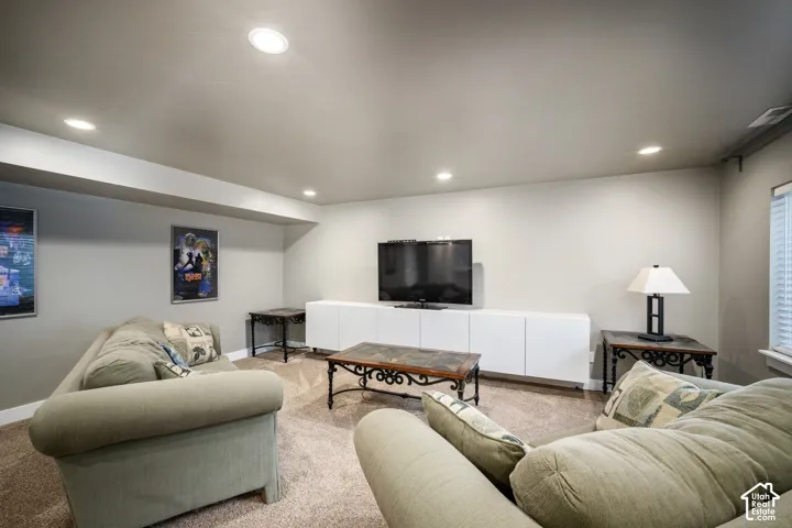 Finished basement recreation room featuring recessed ceiling lighting, neutral carpeting, and a wall-mounted flat-screen television above white cabinetry with open shelving