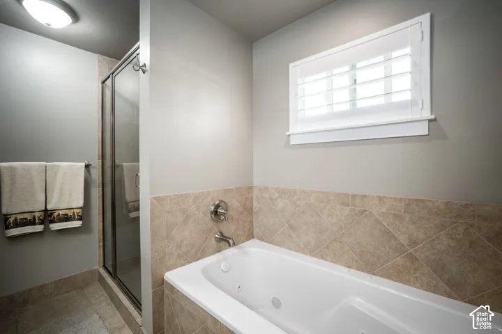 Spa-inspired primary bathroom featuring a soaking tub with integrated jets, frameless glass shower enclosure, tile surround in neutral stone finish, dual vanity with chrome fixtures, recessed ceiling lighting, and a high transom window providing natural l