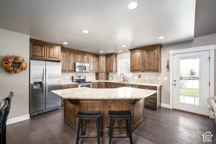 Kitchen featuring wood cabinetry, stainless steel appliances, a multi-sided island with a light-toned countertop, recessed lighting, and wood-finish flooring
