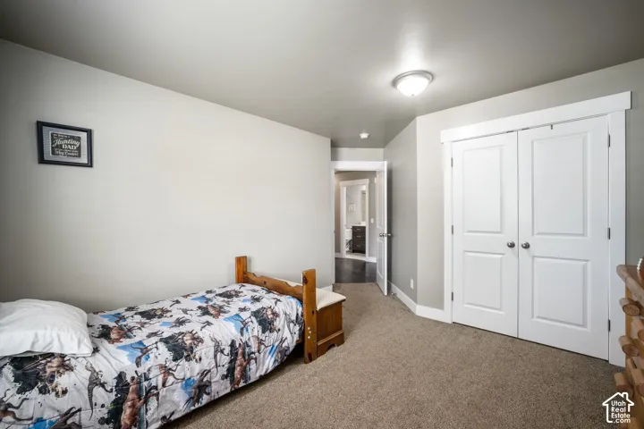 Spacious bedroom featuring carpeted flooring, wood-frame twin bed, double-door white closet with panel detailing, ceiling-mounted light fixture, and direct access to an ensuite bathroom