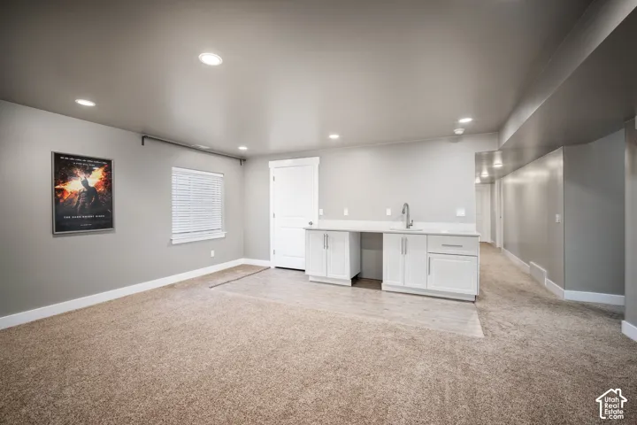 Spacious finished basement featuring neutral carpet flooring, recessed lighting throughout, and a wet bar with white cabinetry and stainless steel sink