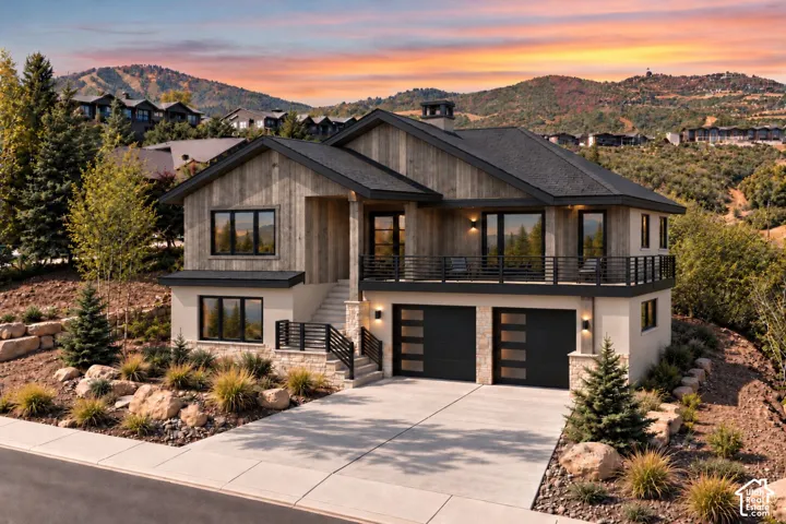 Contemporary residence featuring vertical wood-finish siding, stone accents, a second-story wrap-around balcony with metal railing, two-car garage with glass-paneled doors, and concrete driveway