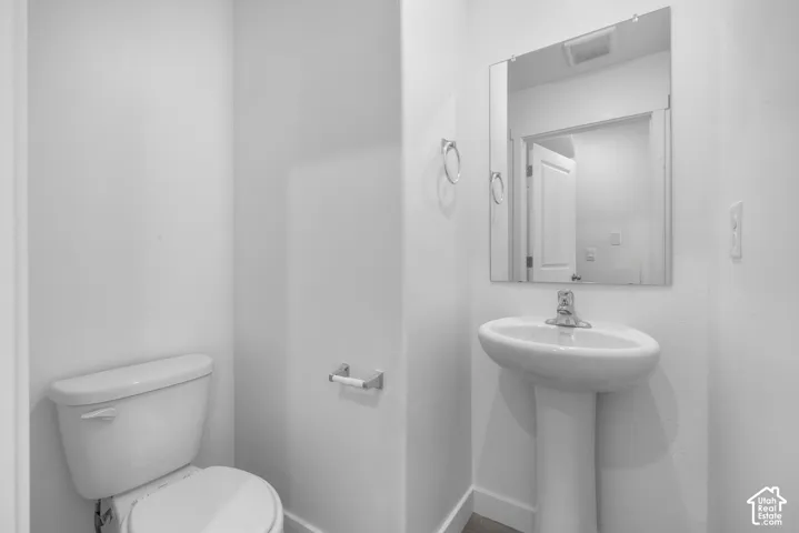 Pedestal sink with chrome faucet, wall-mounted mirror, and white toilet