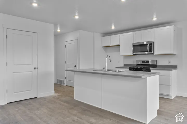 Kitchen featuring white cabinetry, stainless steel appliances, a center island with sink, grey countertops, and wood-finish flooring