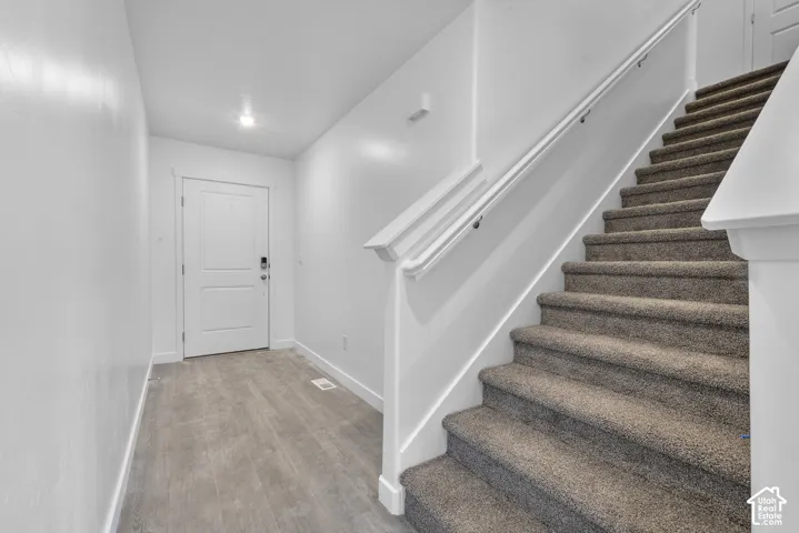 Wood-finish flooring, white paneled door, flush-mount lighting, carpeted staircase, and white handrail