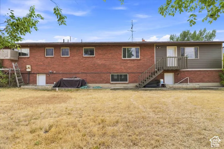 Brick exterior with contrasting siding, wood-finish exterior staircase with railing, multiple windows, and a ground-level access door