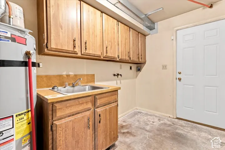 Utility space featuring a laundry sink, wood-finish cabinetry, and a water heater