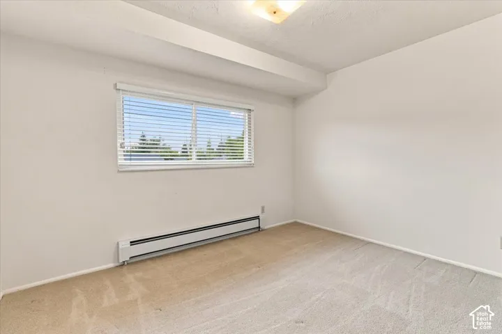 Neutral wall finishes with a window featuring horizontal blinds, carpeted flooring, and a baseboard heating unit