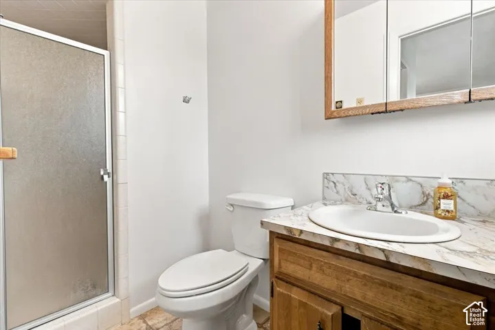 White toilet with a built-in shower featuring a frosted glass door, a vanity with a laminate countertop, an integrated sink, and an overhead mirrored medicine cabinet