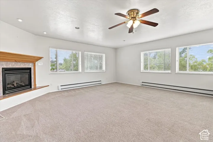 Carpeted room featuring a fireplace with a wood mantel, multiple windows with blinds, a ceiling fan with integrated lighting, and recessed ceiling lights