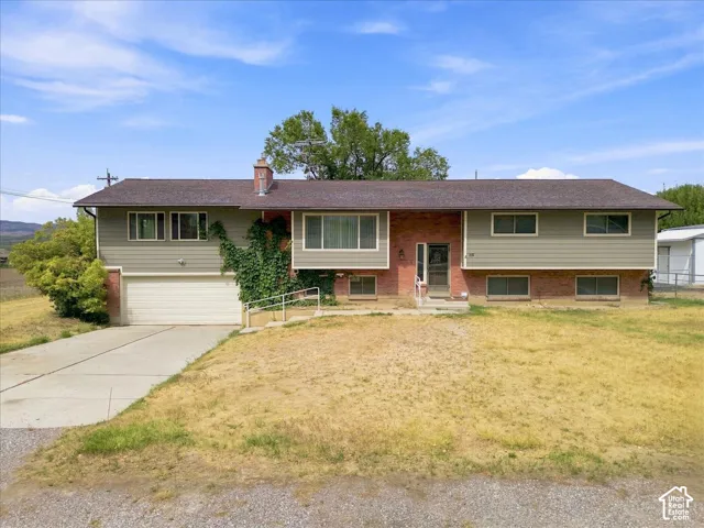 Split-level residence featuring brick and siding facade, an attached garage, paved driveway, and established trees