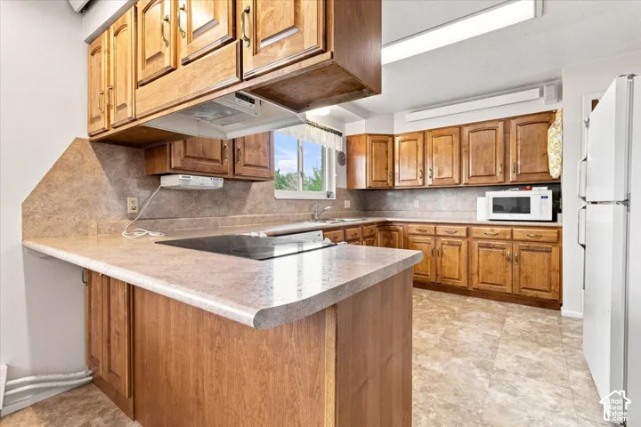 U-shaped kitchen featuring wood cabinetry, integrated cooktop, laminate countertops, and vinyl flooring
