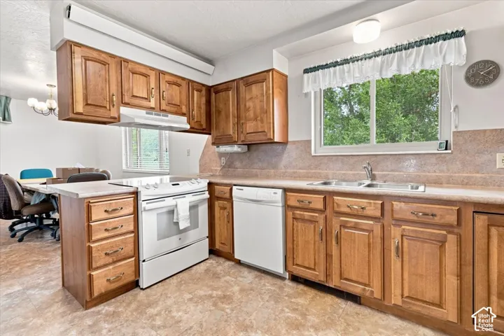 Wood-finish cabinetry with brass hardware, white appliances, and a double basin sink