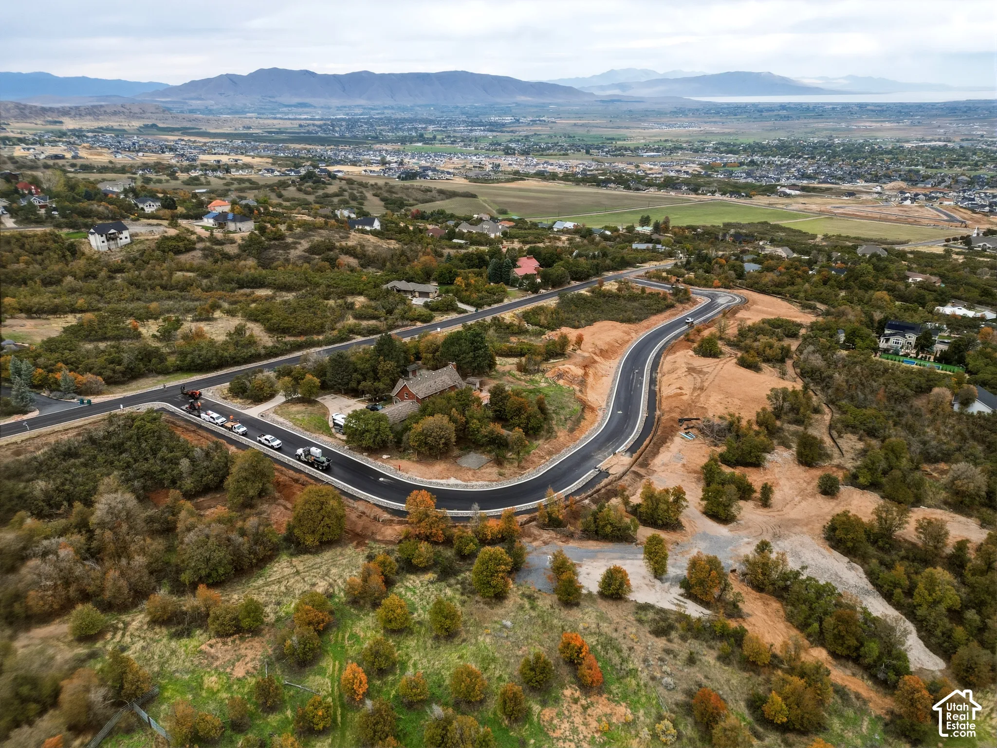 Expansive landscape featuring newly paved roads, undeveloped land, scattered residential structures, and distant mountains
