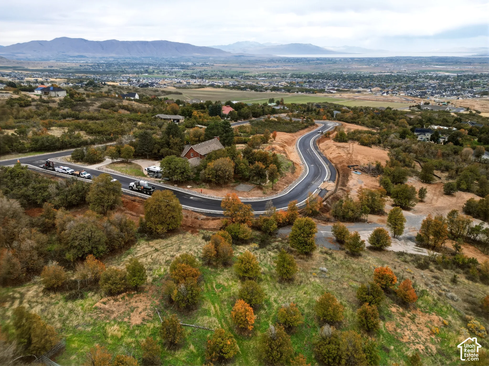 Expansive undeveloped land with a newly paved road, surrounded by deciduous trees and distant mountain ranges