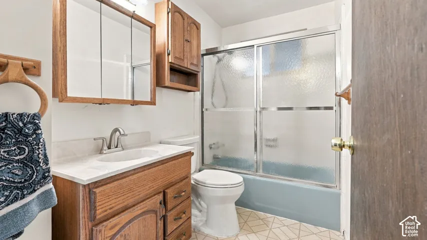 Bathroom featuring a wood-finish vanity with a stone countertop, wall-mounted wood cabinetry, and a tub-shower combination enclosed by sliding textured glass doors
