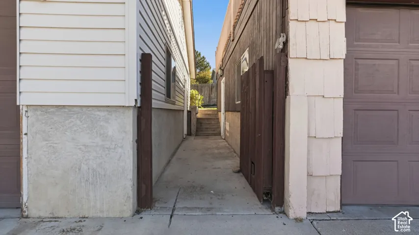 Concrete walkway with wood privacy paneling, finished foundation walls, and integrated exterior staircase