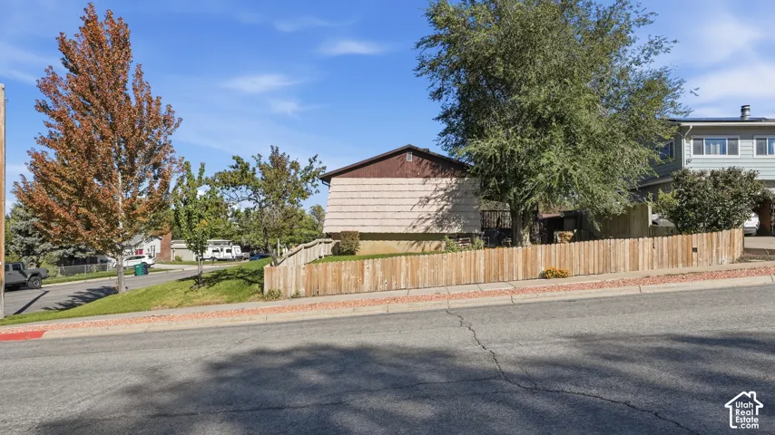 Corner lot exterior featuring a wood-panel fence, mature landscaping, and mature trees