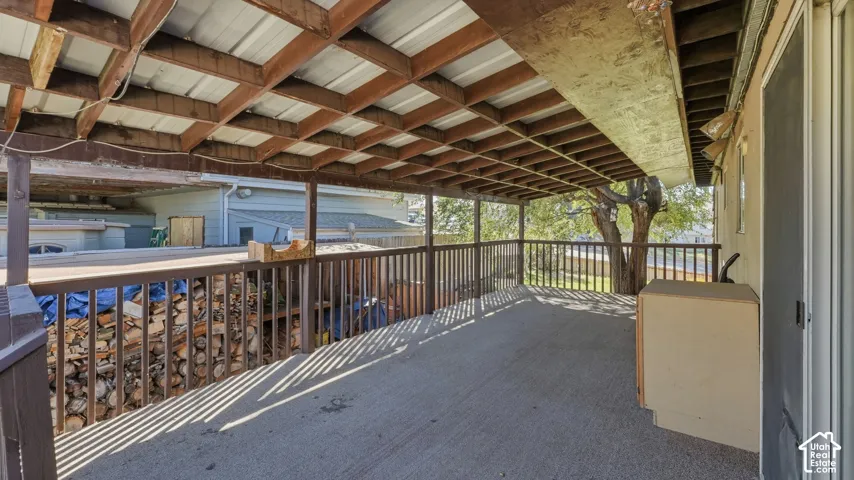 Covered outdoor deck featuring a concrete surface, exposed wood rafters, and vertical wood railing