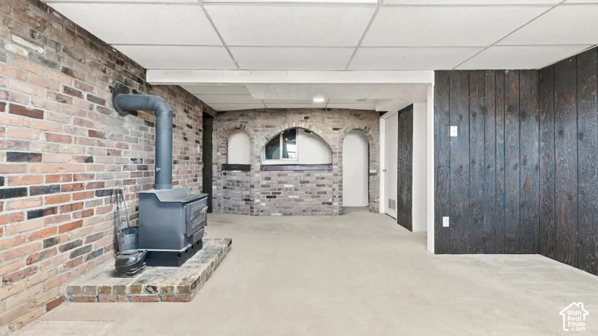 Interior space featuring an exposed brick accent wall, a cast-iron wood-burning stove on a raised brick hearth, custom arched brick niches, and vertical dark wood-paneled wall detailing