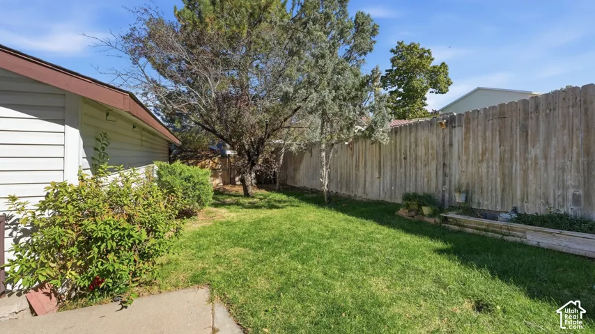 Backyard featuring a grass lawn, mature trees, wood privacy fencing, and a tiered garden bed