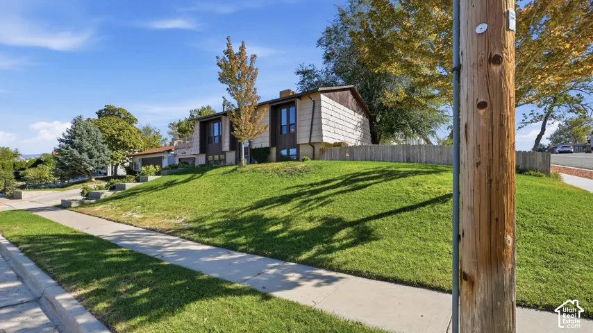 Multi-level residence featuring textured exterior siding, concrete retaining walls, and established trees on a corner, sloped lot with concrete sidewalks