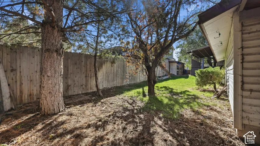 Side yard featuring a perimeter wood privacy fence, mature trees, and a grass lawn