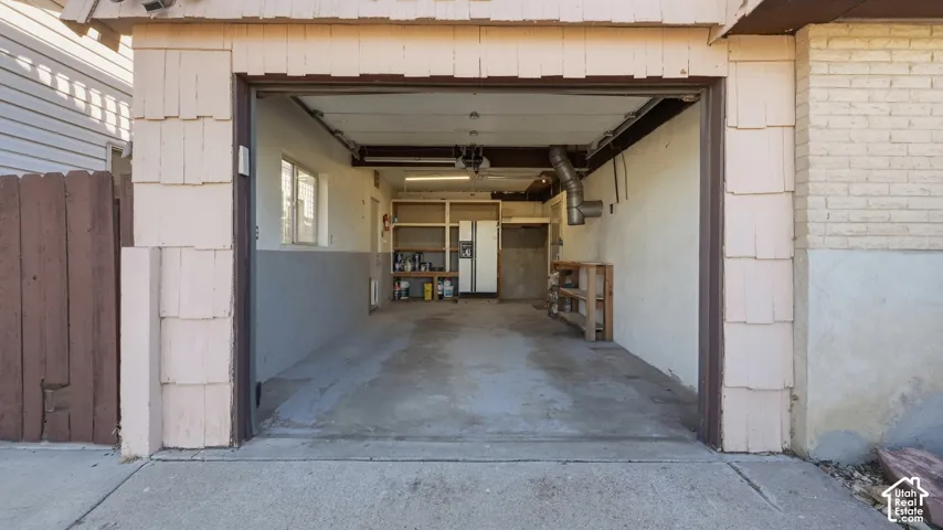 Garage featuring integrated wooden shelving units, concrete flooring, exterior wood-shingle siding, and a white brick facade
