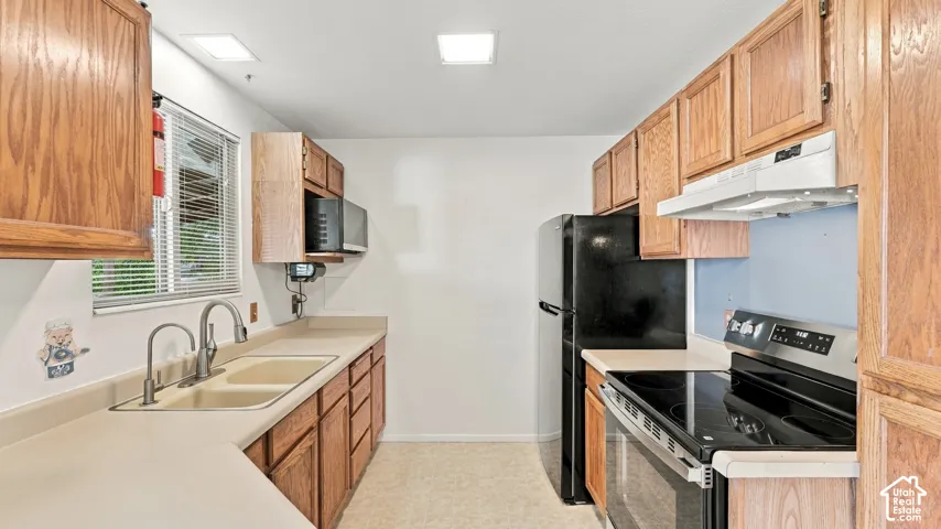 Kitchen featuring oak-finish cabinetry, neutral solid-surface countertops, dual-basin sink with pull-down faucet, and black kitchen appliances