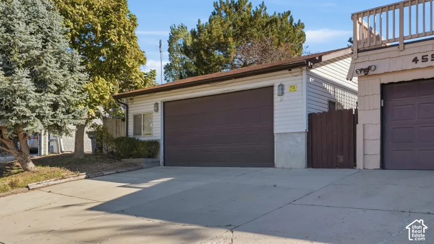 Detached garage featuring horizontal siding, a paneled overhead door, exterior wall-mounted lighting, and a paved concrete driveway