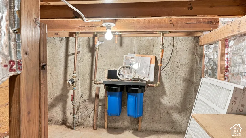 Dual-cartridge water filtration system featuring copper plumbing lines mounted to a concrete foundation wall with exposed wood-frame ceiling joists