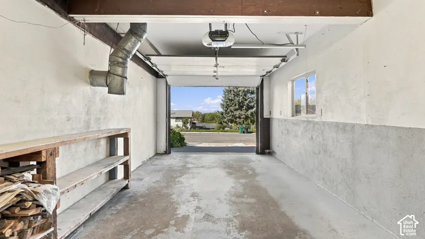Garage featuring concrete flooring, built-in wooden shelving, a side-wall window, and an automatic door opener
