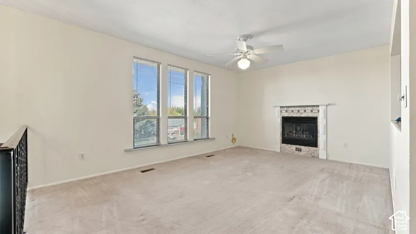 Fireplace with a brick-patterned surround, triple window configuration, ceiling-mounted light fixture with fan, and iron-style railing