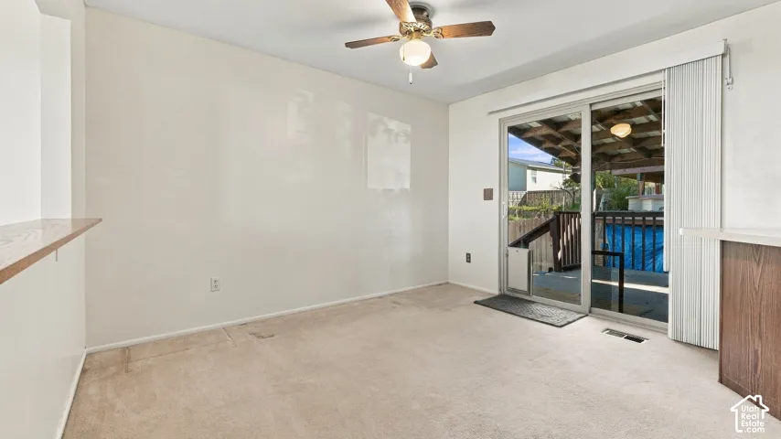 Dining room featuring neutral carpeting, ceiling fan with integrated lighting, wood-finish breakfast bar, and glass sliding door opening to an outdoor deck