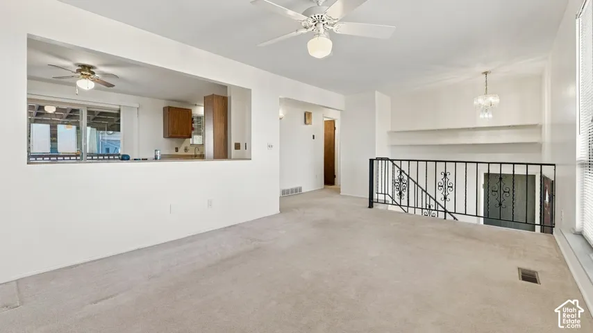 Carpeted room featuring an open-wall pass-through, a ceiling fan, a decorative wrought-iron railing, and built-in wall shelving