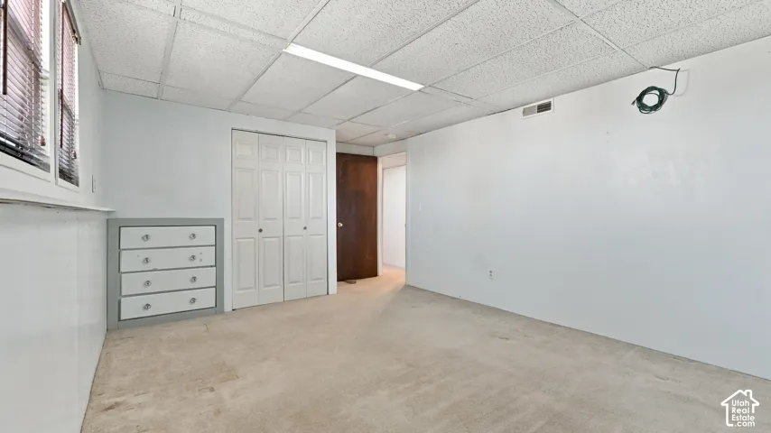 Room featuring neutral carpeting, a built-in cabinetry unit with drawers, white bi-fold closet doors, and a drop ceiling with integrated linear lighting