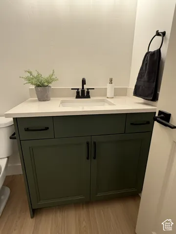 Green vanity with black hardware, white rectangular basin, light-colored countertop, and wood-finish flooring
