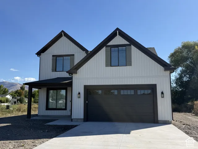 Modern farmhouse exterior with white vertical siding, dark trim, a covered entry, an attached garage, and a concrete driveway