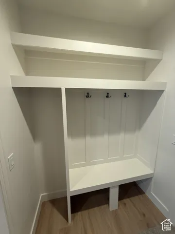 Built-in mudroom bench with upper shelving and coat hooks, featuring wood-finish flooring