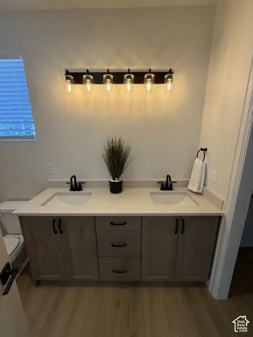 Dual vanity with light-toned countertop, integrated sinks, wood-finish cabinetry, and matte black fixtures