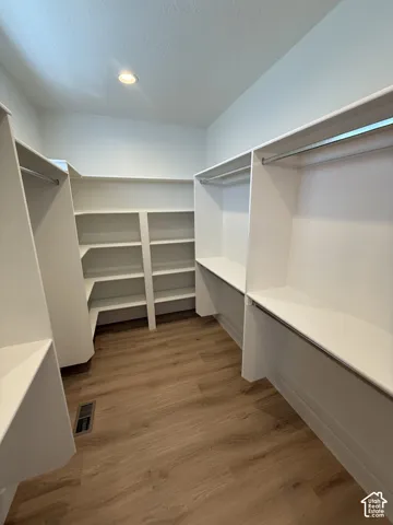 Expansive walk-in closet featuring wood-finish flooring, recessed lighting, white built-in shelving, and hanging rods