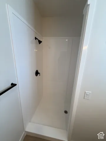 Shower enclosure featuring white paneling, matte black shower head, matte black controls, and a built-in shower pan