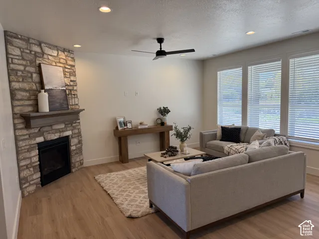 Stone-clad fireplace with mantel, recessed lighting, ceiling fan, wood-finish flooring, and multiple windows with blinds