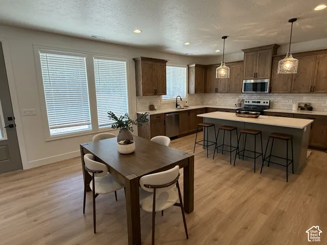 Open-concept kitchen featuring wood-finish flooring, wood cabinetry, stainless steel appliances, and a central island with countertop seating