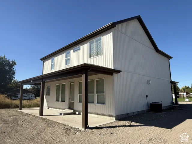 Two-story exterior with vertical siding, covered patio, multiple windows, and dark gutters